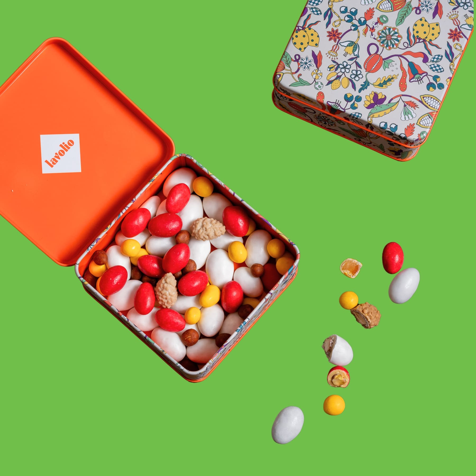 Colorful candy mix avolio in an open tin with a colorful lid on a green background