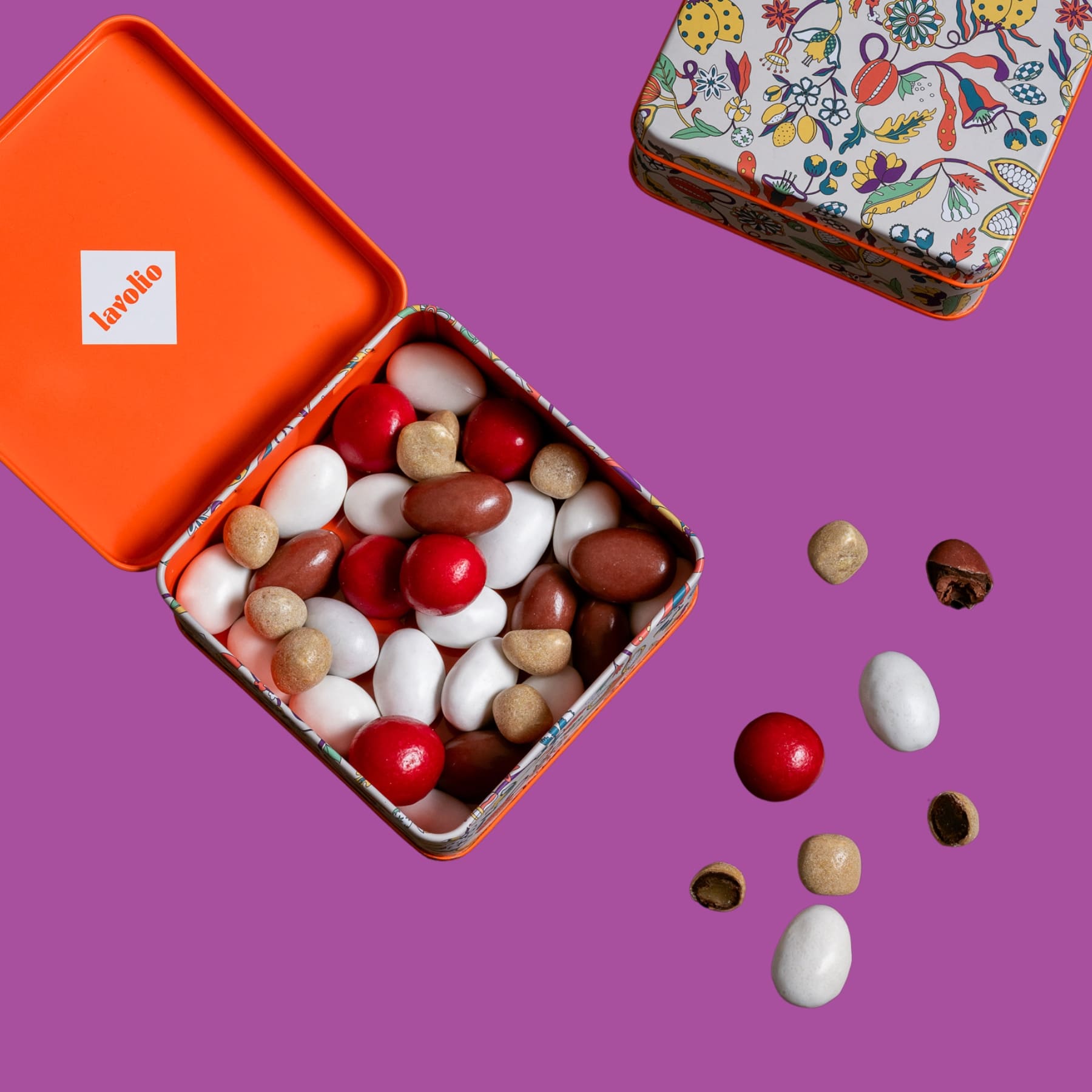 Open tin of colorful candies lavolio with a decorative lid on a purple background