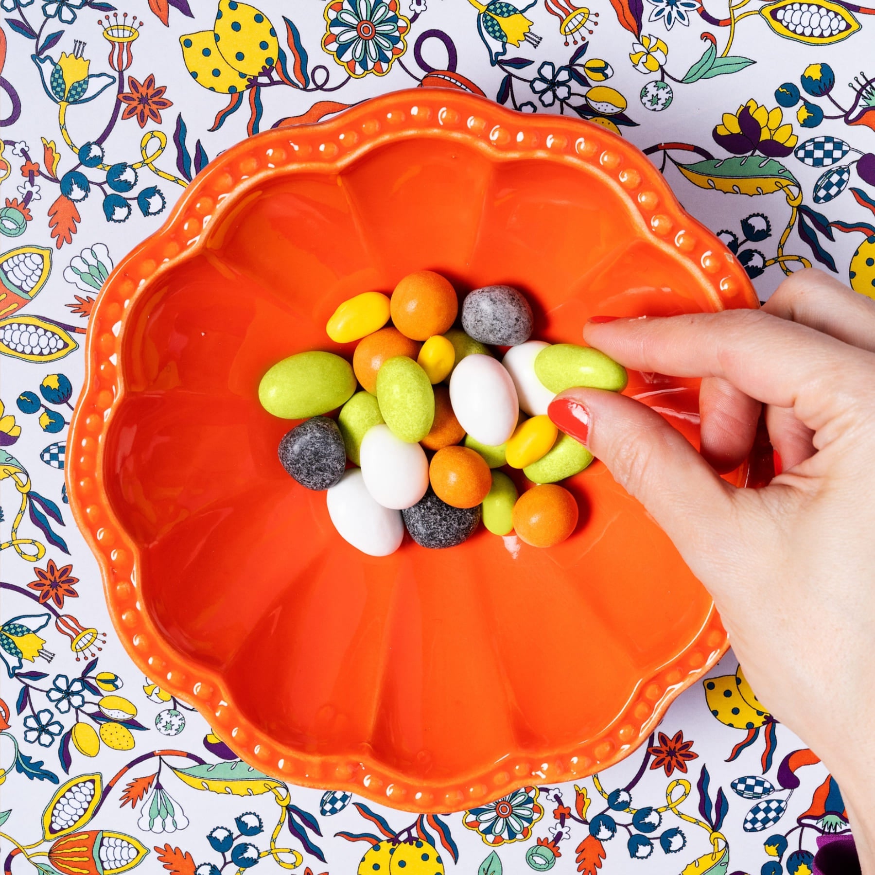 Hand picking colorful candies from an orange bowl on a patterned background