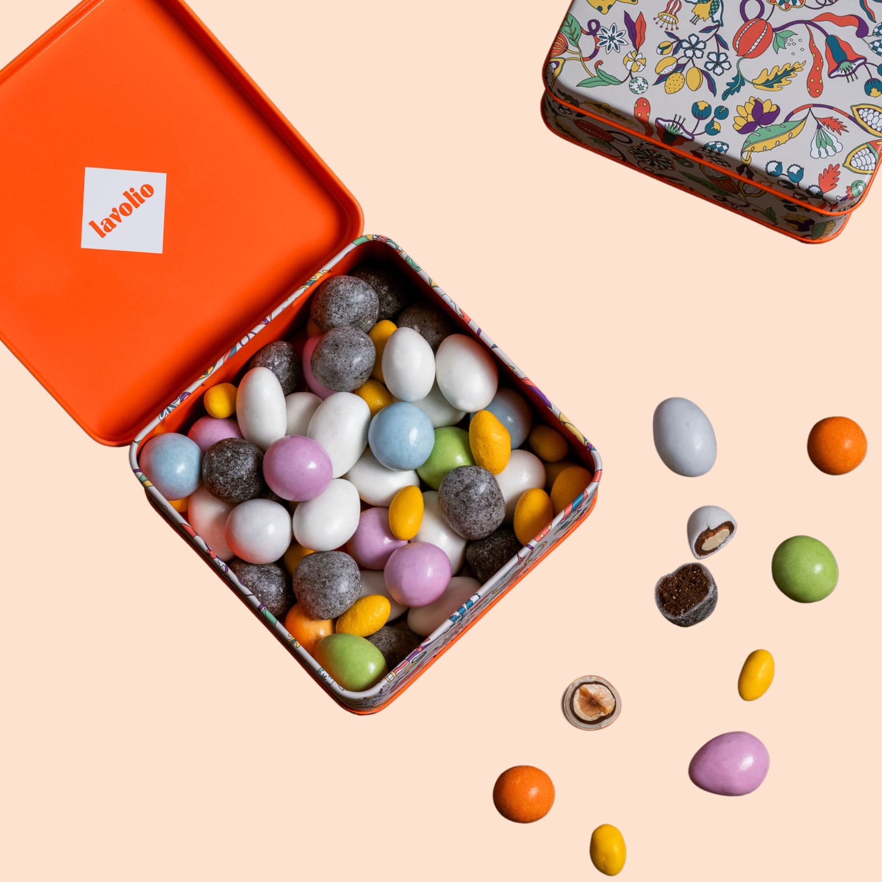 Open tin of colorful candies lavolio with a decorative lid on a peach background