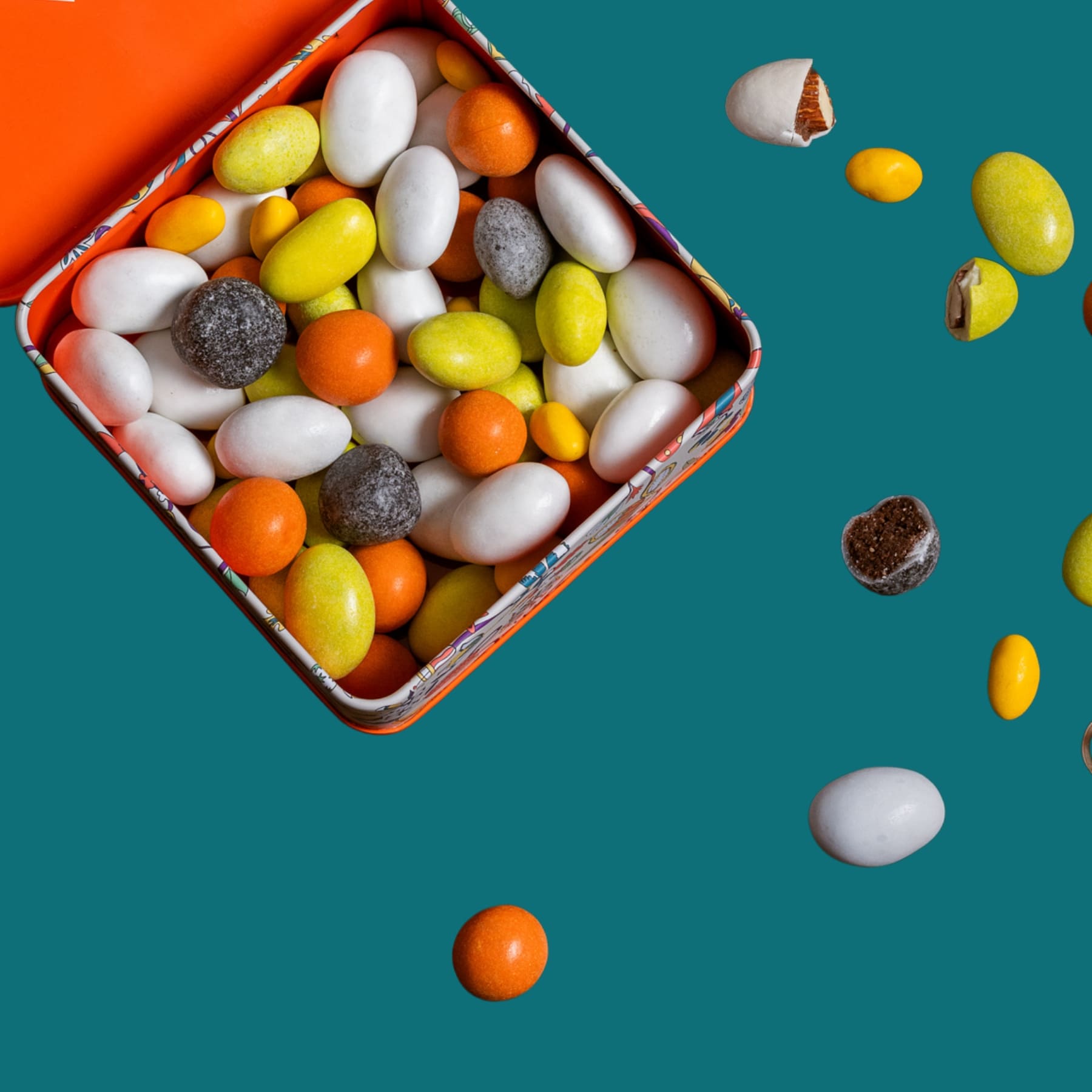 Colorful candy assortment spilling out of an open lavolio orange tin box on a teal background