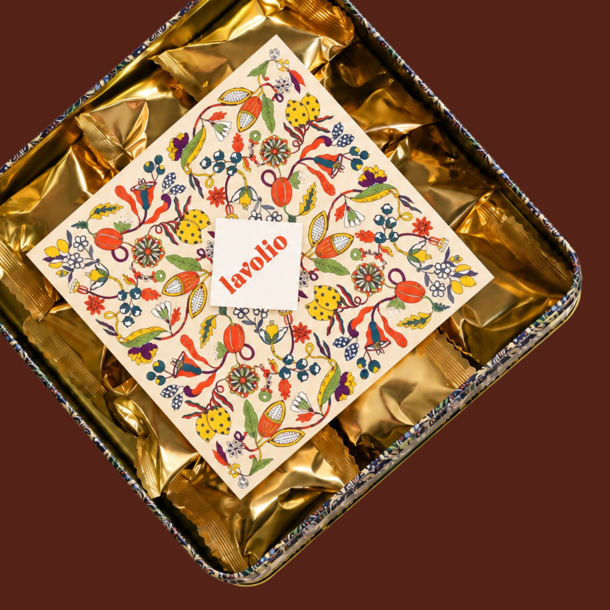 A square foil gift box lined with shiny gold paper, featuring a decorative cream card with a colorful Lavolio pattern.