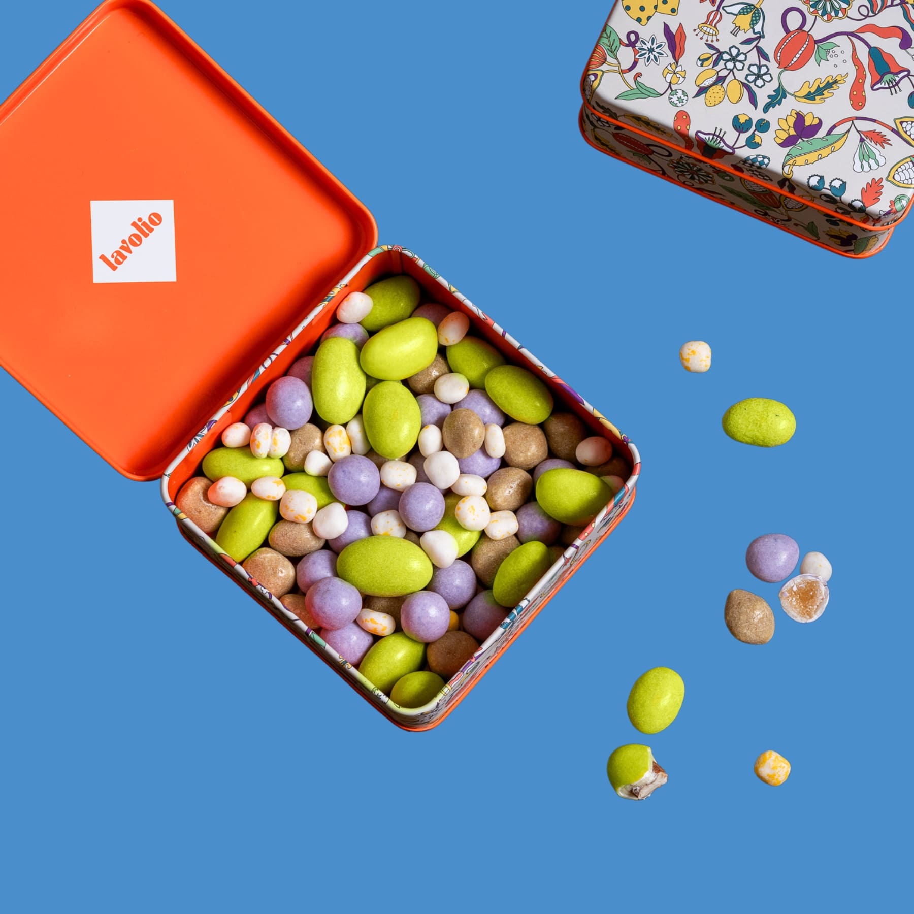 Colorful candy assortment spilling out of an open lavolio orange tin box on a blue background